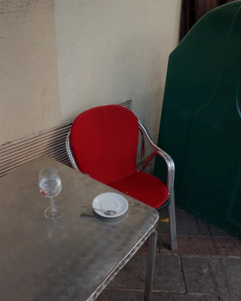 Cantes de ida y vuelta, de Ana Suanes: silla roja junto a una mesa de terraza con una copa y un plato vacío